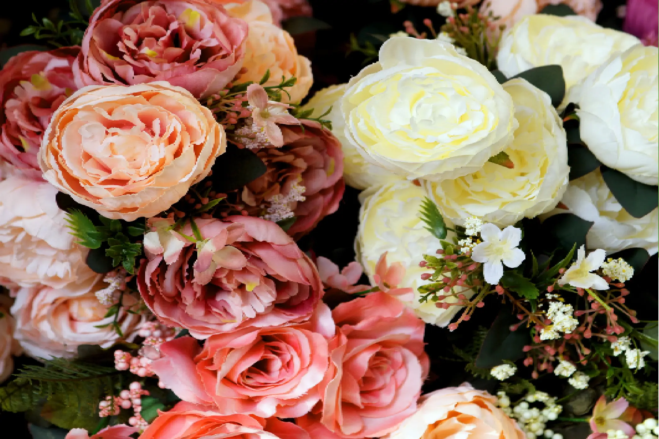 A close-up of assorted artificial flowers in shades of pink, peach, cream, and white with green foliage and small white accent flowers.